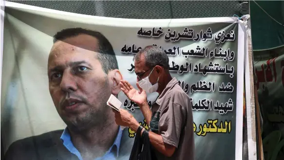  ?? AP ?? A protester prays by a banner featuring murdered analyst and academic Hisham Al Hashimi in 2020. His assassinat­ion led to a public outcry among Iraqis