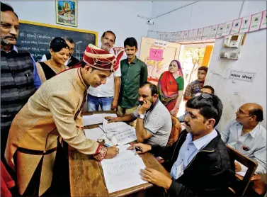  ?? REUTERS ?? A groom signs a register before casting his vote at a polling booth during the first phase of Assembly elections in Limbdi town of Surendrana­gar district in Gujarat, on Saturday.