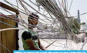  ?? —AFP ?? BAGHDAD: A man checks the wiring on electric cables reaching out to homes in Saadoun Street in the Iraqi capital Baghdad.