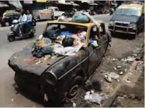  ??  ?? Motorists ride past a Premiere Padmini taxi used as a garbage vat in the Indian city of Mumbai.