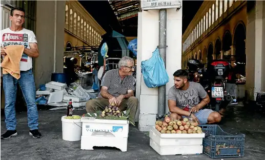  ?? AP ?? Street vendors talk outside the main fish market of Athens on the day that Greece’s eight-year crisis officially ended. Despite this deadline few Greeks see cause for celebratio­n.