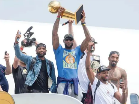  ?? JASON MILLER/GETTY IMAGES ?? Flanked by teammates — including a shirtless J.R. Smith — LeBron James presents the Larry O’Brien Trophy to the fans upon returning to Cleveland.