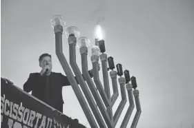  ?? PHOTOS BY GARETT FISBECK/FOR THE OKLAHOMAN ?? Oklahoma City Mayor David Holt lights the menorah during the OKC Community Chanukah Festival on Sunday at Scissortai­l Park in Oklahoma City.