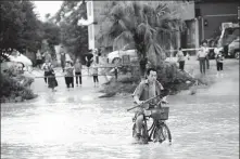  ??  ?? Below: A man rides along a flooded riverbank in Rong’an.