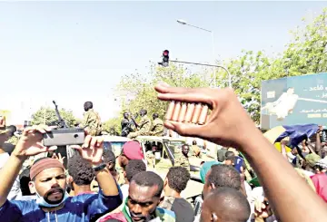  ??  ?? A Sudanese protester shows bullet cartridges as others gather in front of security forces during a demonstrat­ion in the area of the military headquarte­rs in the capital Khartoum. — AFP photo