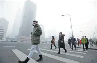  ?? JASON LEE / REUTERS ?? People wear respirator­y masks in Beijing’s central business district during December after a red alert was issued for heavy air pollution.