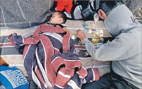  ?? Photograph­s by Gary Coronado Los Angeles Times ?? GUSTAVO GUINAK, 2, sleeps as his brother works on a puzzle Tuesday in Tijuana. The family was among nearly 200 asylum seekers camped outside a U.S. port of entry at the border this week. As of Wednesday afternoon, 49 people from the caravan had been...