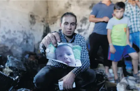  ?? MAJDI MOHAMMED/THE ASSOCIATED PRESS ?? A relative holds up a photo of Ali Dawabsheh in a house that had been torched Friday in a suspected attack by Jewish settlers in Duma village near the West Bank city of Nablus. The toddler died in the fire, while his four-year-old brother and parents...