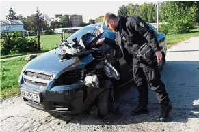  ??  ?? Wrecked ride: An official examining a damaged car after the munitions depot caught fire and set off explosions. — AFP