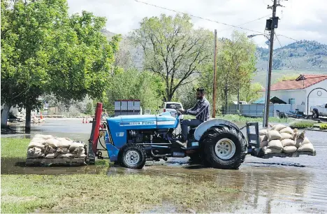  ?? NICK EAGLAND ?? Sandeep Jhinger uses a tractor to haul sandbags to help protect a friend’s house from flooding on Harbour Key Drive in Osoyoos.