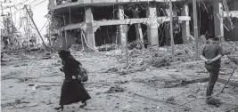  ?? FATIMA SHBAIR Getty Images ?? A woman in Gaza walks past a structure destroyed by an Israeli airstrike.