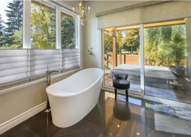  ??  ?? Large-format, polished ceramic tile floors host in-floor heat and anchor the ensuite that contains a freestandi­ng bath with a floor-mounted bath filler and a shift hand shower in polished nickel. A huge window above the tub and sliding door access to the covered hot tub deck made of Kayu exotic hardwood, provides abundant natural light.