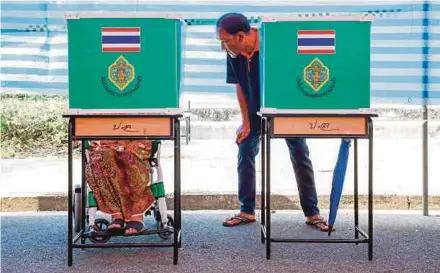  ?? EPA PIC ?? A man offering help to a woman in a wheelchair filling out her ballot at a polling station in the general election on the outskirts of Bangkok, Thailand, yesterday.