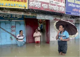  ?? — AFP ?? Shopkeeper­s stand in a flooded street next to their stores after a heavy downpour brought flooding to Agartala on Monday.