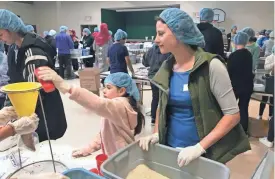  ?? JACOB CARPENTER / MILWAUKEE JOURNAL SENTINEL ?? Alana Hammer watches as her 8-year-old daughter, Auden, pours a cup of rice into a package of food destined for Syrian refugees in Jordan.