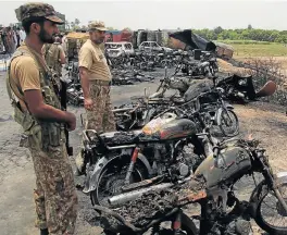  ??  ?? Inferno: Pakistani soldiers stand guard beside burnt-out vehicles at the scene where an oil tanker caught fire following an accident on a highway near the town of Ahmedpur East, about 670km from Islamabad, on Sunday. At least 140 people were killed.