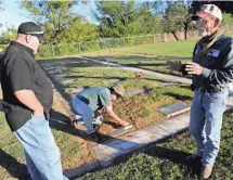  ?? RONALD W. ERDRICH ?? John Trigg, right, speaks with Flint Knight as Tommy Gordon cleans a marker at Breckenrid­ge Cemetery.