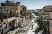  ?? IVOR PRICKETT / THE NEW YORK TIMES ?? A fighter with the Syrian Democratic Forces, an American-backed, Kurdish-led group, walks past damaged buildings in Raqqa, Syria, a former Islamic State stronghold.