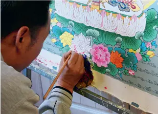  ??  ?? A thangka artist is focused on the details of his work.