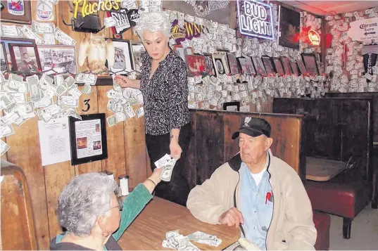  ?? JOHN LARSON/EL DEFENSOR CHIEFTAIN ?? Leo Murphy, left, helps Janice Argabright remove some of the currency from the wall of the historic Owl Bar and Café Monday, as Adolph Baca, right, oversees the counting of the year’s worth of ones, fives, tens, twenties and even a $100 bill left by...