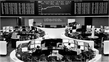  ?? — Reuters photo ?? Traders work in front of the German share price index, DAX board, at the stock exchange in Frankfurt, Germany. After buying big American brands like Apple, Pepsi and Yahoo!, activist shareholde­rs – investors in search of big dividends - now are setting...