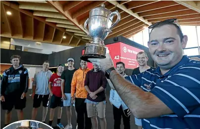  ??  ?? Nelson Griffins coach Ryan Edwards holds the Hawke Cup aloft with the team at Nelson Airport; left, Edwards embraces Dave Leonard, right, general manager of Nelson Cricket.