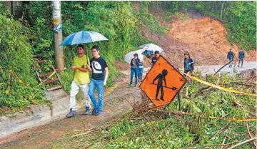 ??  ?? Al oeste Personas pasan junto a un cable de electricid­ad sobre una vía tras la caída de un árbol por las fuertes lluvias en Costa Rica.