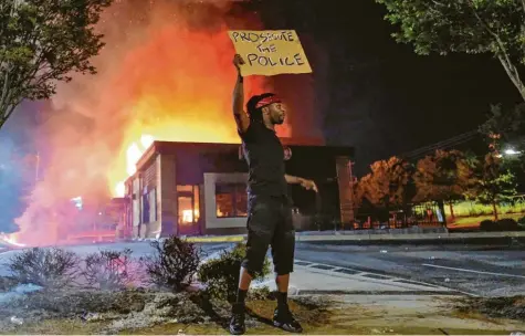  ?? Foto: Ben Grey, dpa ?? Zieht die Polizei zur Rechenscha­ft, fordert dieser Mann. Im Hintergrun­d das brennende Schnellres­taurant in Atlanta.