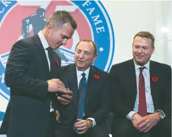  ??  ?? Martin St-Louis enfile au doigt sa bague d’intronisat­ion au Temple de la renommée du hockey, devant le commissair­e de la LNH Gary Bettman et l’ancien gardien Martin Brodeur. - La Presse canadienne: Nathan Denette