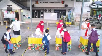  ??  ?? Pupils at SK St Thomas line up for body temperatur­e screening prior to being allowed to enter class, during the reopening of schools in Kuching, Samarahan and Padawan on Aug 17.