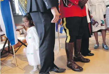  ??  ?? Three-year-old Simboo, daughter of Ethiopian refugees who are now Canadian citizens, hides behind dignitarie­s after a citizenshi­p ceremony at the Maritime Museum of the Atlantic in Halifax on Monday.