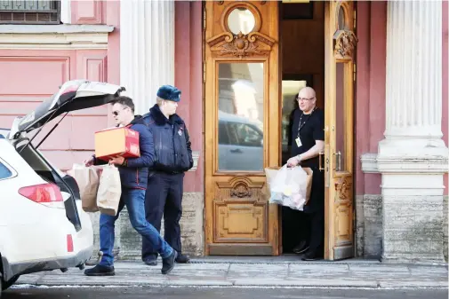  ??  ?? Men carry boxes and packs out from the US Consulate as a Russian police officer guards the entrance, in St.Petersburg, Russia, on Friday. (AP)
