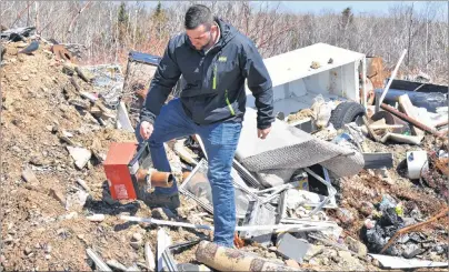  ?? NIKKI SULLIVAN/CAPE BRETON POST ?? Dylan Yates, founder of the Cape Breton Environmen­tal Associatio­n, picks up a burner unit from a furnace he found buried in the mounds of garbage that has been illegally dumped behind the water tower in Reserve Mines. Along with furnace pieces are...