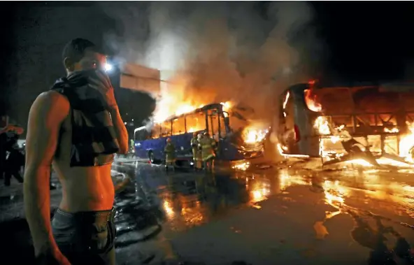  ??  ?? A man covers his face as firefighte­rs tackle buses set on fire by protesters in Rio de Janeiro.