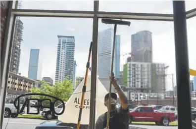  ?? Photos by Aaron Ontiveroz, The Denver Post ?? A man who wished to be identified only as Billy cleans the windows of Tee Lee, a cafe in Five Points, as the backdrop of urban developmen­t rises behind him on nearby streets Wednesday.