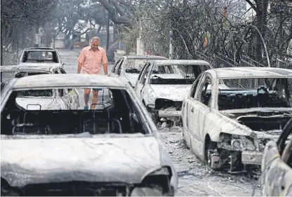  ??  ?? A man passes burned cars in Mati, east of Athens, after wildfires ripped through the area