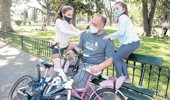  ?? Alejandro Guyot ?? Matías Iuspa responde mensajes de trabajo mientras acompaña a sus hijas Federica y Eugenia a andar en bici en la plaza