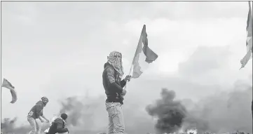  ??  ?? A demonstrat­or holds a Palestinia­n flag during clashes with Israeli troops, near the border with Israel in the southern Gaza Strip. — Reuters photo