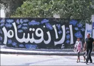  ?? MAHMUD HAMS / AFP ?? A Palestinia­n man and his daughter walk past graffiti that says “Division” in Arabic in Gaza City on Sunday after the deal was announced between Hamas and Fatah.