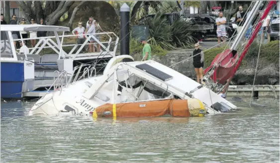  ?? (Photo: AP) ?? Peopleobse­rve at a damaged boat in a marina at Tutukaka, New Zealand, Sunday after waves from a volcano eruption swept into the marina.