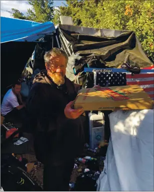  ?? COURTESY ?? A man at a homeless encampment at Interstate 280 and Stevens Creek Boulevard holds a pizza given to him by a group of volunteers who recently donated food and blankets to homeless people in San Jose and Cupertino encampment­s. To create a better donation pipeline for their efforts, the volunteers formed the nonprofit North American Love and Dedication Associatio­n.