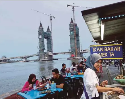 ?? PIC BY GHAZALI KORI ?? Diners enjoying a meal at a food stall with the Sungai Terengganu drawbridge in the background yesterday.