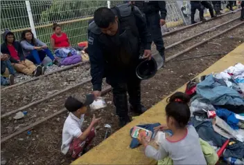  ?? AP PhOtO/MOISeS CAStIllO ?? Guatemalan police officer gives a migrant child some food as the migrants bound for the U.S.-Mexico border wait on a bridge that stretches over the Suchiate River, connecting Guatemala and Mexico, on Saturday.