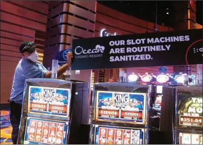  ?? (AP/Wayne Parry) ?? A worker at the Ocean Casino Resort in Atlantic City, N.J., installs a sign earlier this month about slot machines being sanitized to prevent the spread of the coronaviru­s.