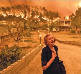  ?? Photo: Bloomberg News ?? An elderly resident reacts as a wildfire rages behind her in the village of Gouves, on the island of Evia, Greece’s second-biggest island, on August 8, 2021.
