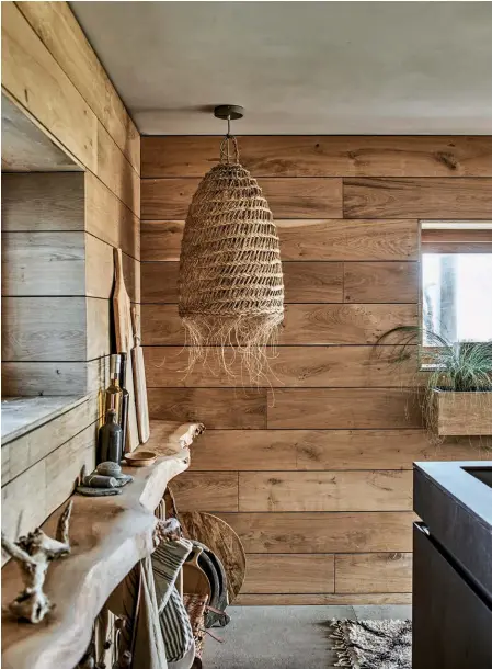  ??  ?? ABOVE At one end of the kitchen, the couple fitted a shelf made from waney (natural live-edged wood) to display their collection­s of found objects and basketware. Statement oversized wicker lighting contribute­s further texture and a relaxed mood. That feeling is continued into the snug area, which is home to a tiled hearth and a free-standing wood-burning stove OPPOSITE The pair created an upstairs living room where they can enjoy uninterrup­ted views over the marshes beyond the garden. The decor has a relaxed Scandi feel. A brick wall has
been left exposed to merge the old parts of the house with the new, and it anchors the muted palette of off-whites and pale greys