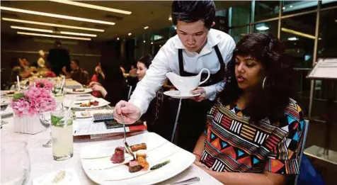  ??  ?? A Taylor’s University student serving the main course, angus filet with asparagus and smoked brisket to a guest at the culinary showcase at the university.