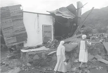  ?? RICKO WAWO/AP ?? Fatal floods, landslides in Indonesia: Nuns walk past a damaged house Tuesday in a flood-affected village on Lembata Island in Indonesia. Multiple disasters caused by torrential rains in eastern Indonesia have killed at least 55 people and displaced thousands, the country’s disaster relief agency said. More than 40 other people were missing.