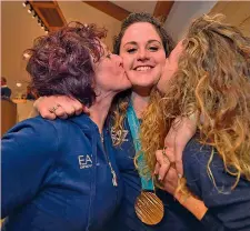  ??  ?? A sinistra Michela Moioli con l’oro al collo a Casa Italia firma l’autografo sul tricolore. A destra viene festeggiat­a da mamma Fiorella e dalla sorella Serena ANSA