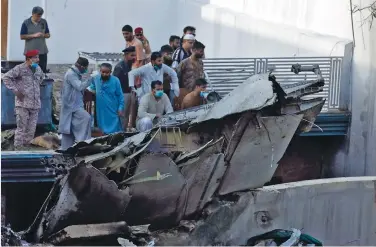  ?? (Akhtar Soomro/Reuters) ?? PEOPLE STAND next to the debris of a Pakistan Internatio­nal Airlines plane after it crashed into a residentia­l area in Karachi on Friday.